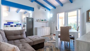 Una sala de estar moderna con un sofá seccional, una zona de comedor con una mesa y sillas, y una cocina con un refrigerador y alacenas.