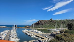 Un puerto deportivo con barcos amarrados, una carretera que conduce al agua y una colina con edificios al fondo.