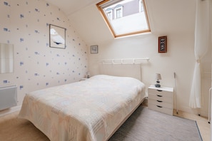 A bedroom with a bed, a radiator, a window, a bedside table, and a nightstand.