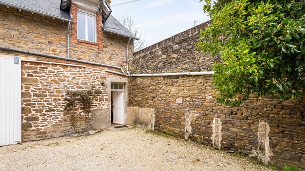 A stone building with a gravel driveway, a white door, and a small tree.