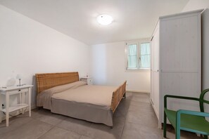 Une chambre à coucher comprenant un lit, une table de chevet, une lampe, une armoire et une fenêtre.