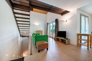 Un salon moderne avec un escalier, un canapé vert, un meuble TV en bois et une porte-fenêtre coulissante.