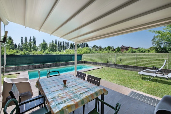 An outdoor patio with a pool, a table, and lounge chairs.