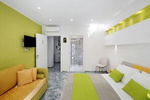Una habitación de hotel moderna con cama, sofá, televisor y zona de ducha.