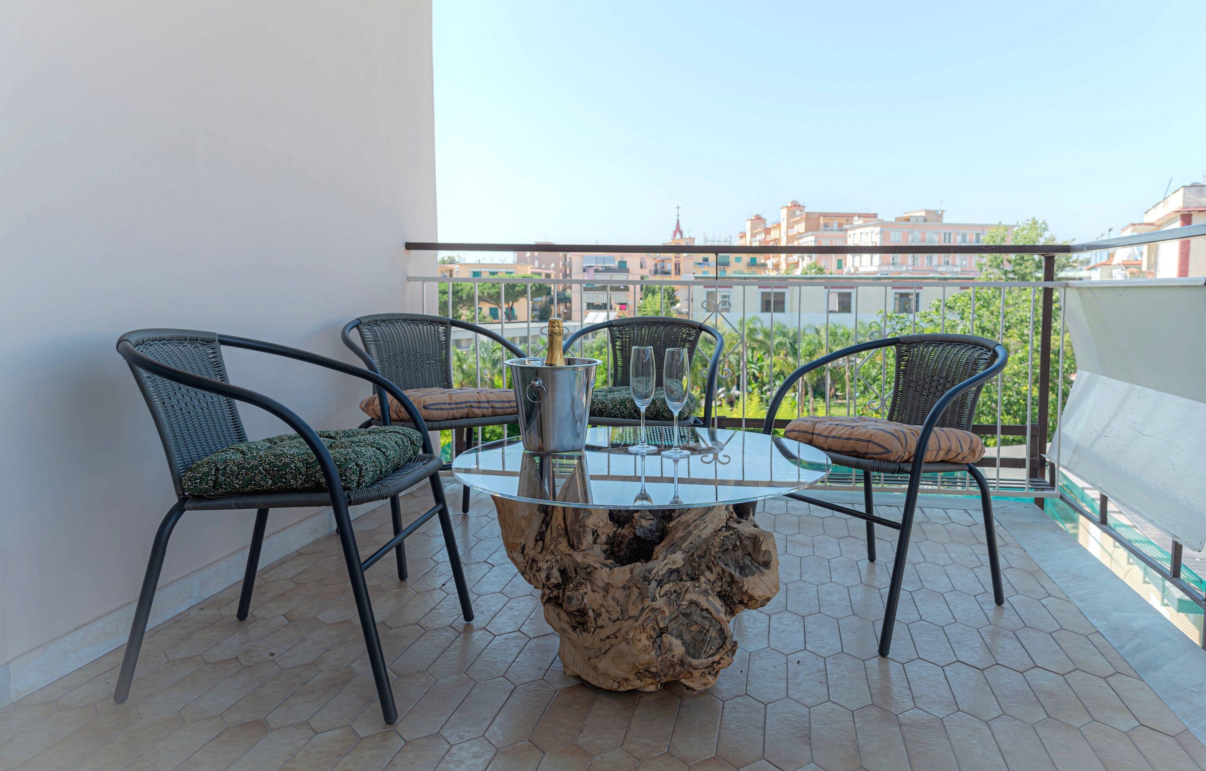 A balcony with a round table, four chairs, and a bottle of champagne.