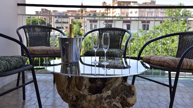 Un balcón con una mesa redonda de cristal, dos sillas, un cubo de metal y dos copas de vino.
