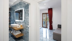 Un baño moderno con lavamanos de mármol, repisas de madera y puerta de vidrio a un balcón.