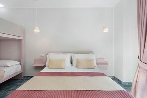 A bedroom with a bunk bed, a large bed with a red and beige bedspread, bedside tables, and pendant lights.