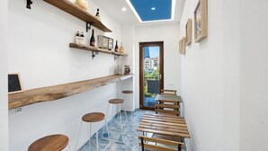 Un pasillo estrecho con estantes de madera, taburetes y mesas, que conduce a una puerta con vistas a edificios.