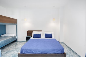 A room with a bunk bed, a single bed with a blue bedspread, two bedside tables, and two wall-mounted lights.