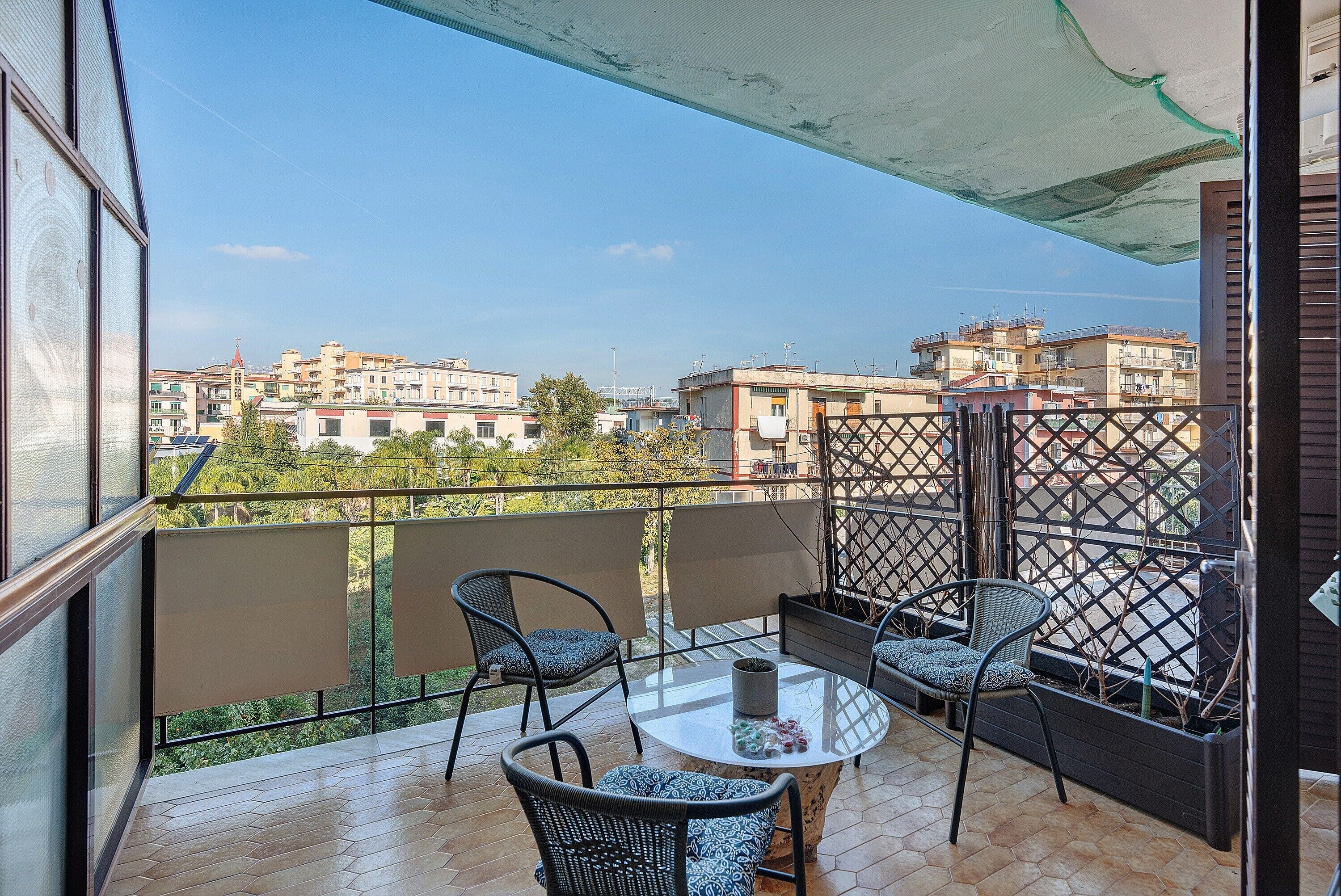 Un balcón con una mesa y sillas, vista a edificios y un toldo protector.