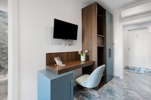 A modern room with a mounted TV, a desk with a telephone, a chair, and a cabinet.