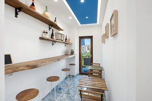 A narrow hallway with wooden shelves, stools, and tables, leading to a door with a view of buildings.