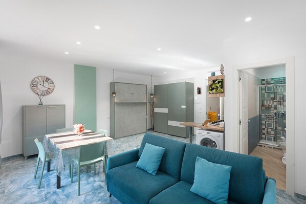 Una sala de estar moderna con sofá, mesa de comedor y una zona de cocina con lavadora.