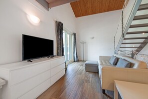 Un salon moderne doté d’un téléviseur à écran plat, d’un canapé, d’un banc, d’un escalier et d’une grande fenêtre.