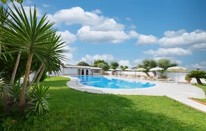 Una piscina circondata da un'area verdeggiante, un piccolo edificio e un cielo sereno.