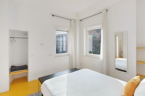 Une chambre à coucher avec un lit, un banc, un porte-manteau mural et deux fenêtres.