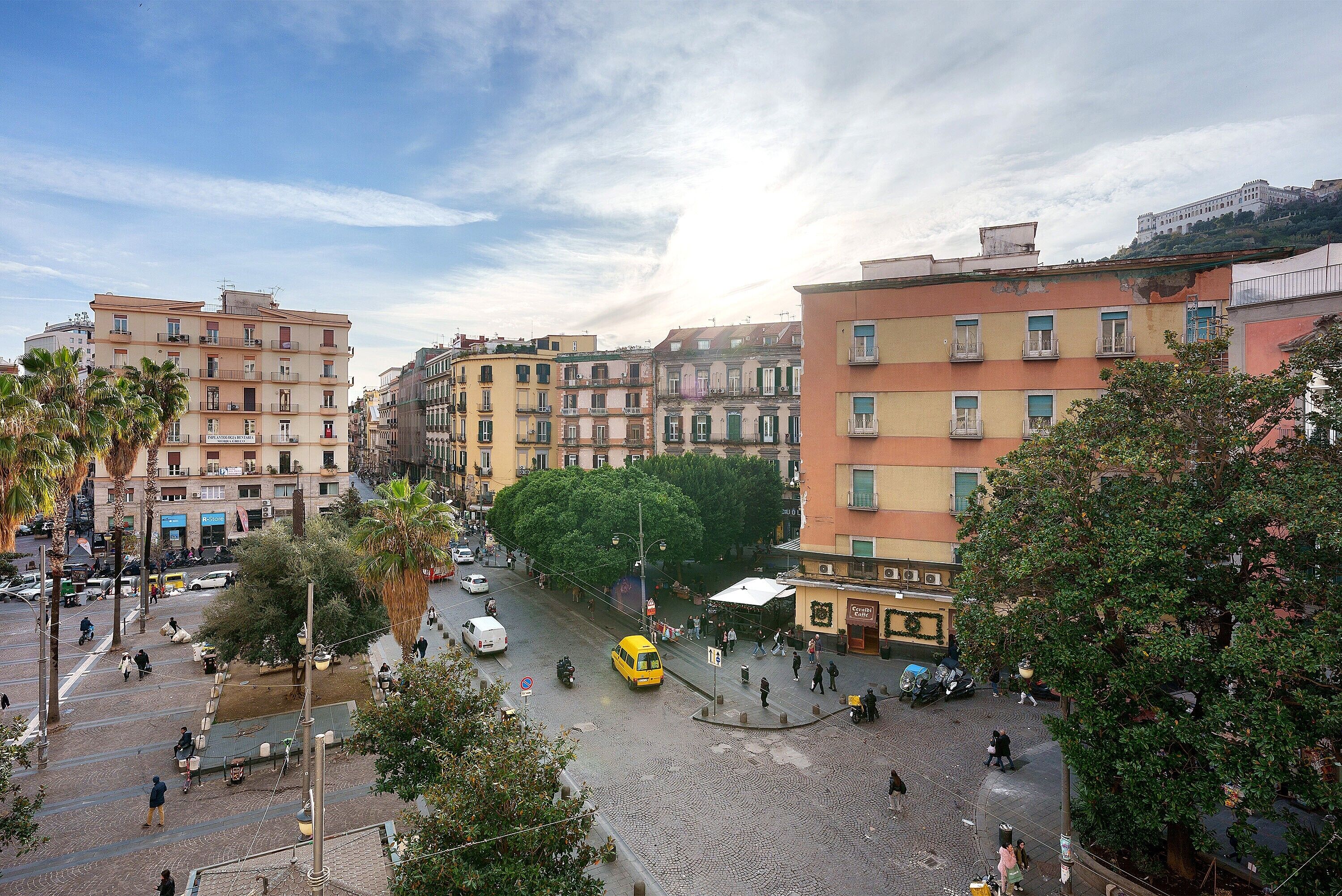 Una plaza urbana con edificios, una camioneta amarilla y peatones.