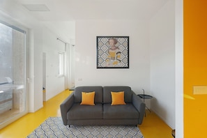 Un salon moderne avec un canapé gris, deux coussins orange, un tapis à motifs et une œuvre d’art accrochée au mur.