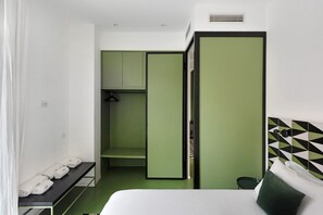 Una habitación de hotel con cama, un armario verde, un banco con toallas y una mesita.