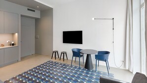 A modern living room with a flat-screen TV, a round table, blue chairs, a patterned rug, and a ceiling light. - Apartment 'Deluxe In Via Toledo' with Balcony, Wi-Fi and Air Conditioning (Napoli)