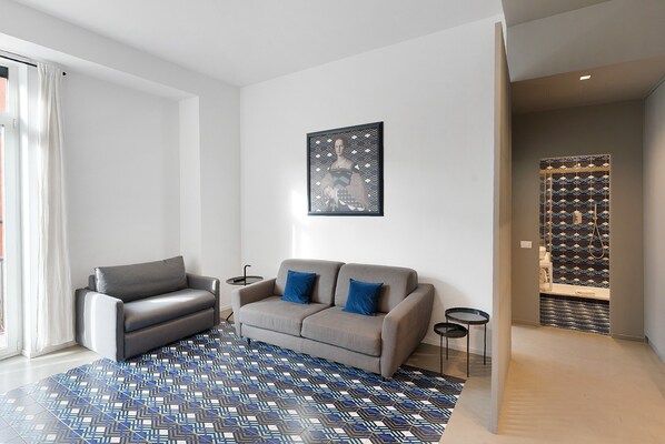 Un salon moderne avec un canapé gris, des coussins bleus, un tapis à motifs et une œuvre d’art encadrée accrochée au mur.