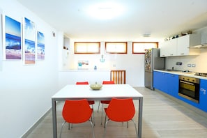 A modern kitchen with a white table and red chairs, blue cabinets, and a view of the sea through the windows. - Villa 'With Pool in Private Park' with Sea View, Wi-Fi and Air Conditioning (Agnone Cilento)
