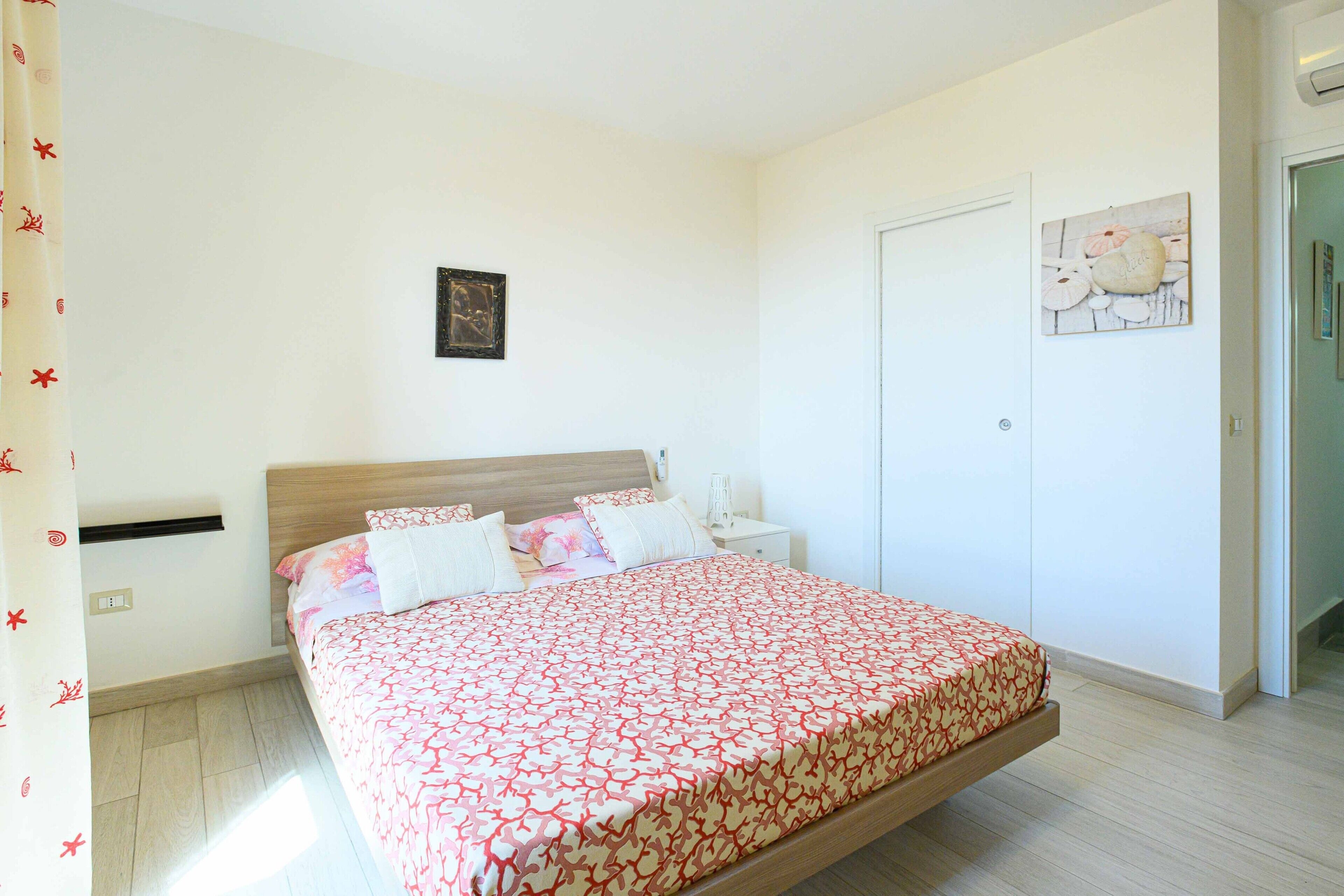 Un dormitorio con cama, mesitas de noche, un cuadro en la pared y una puerta.