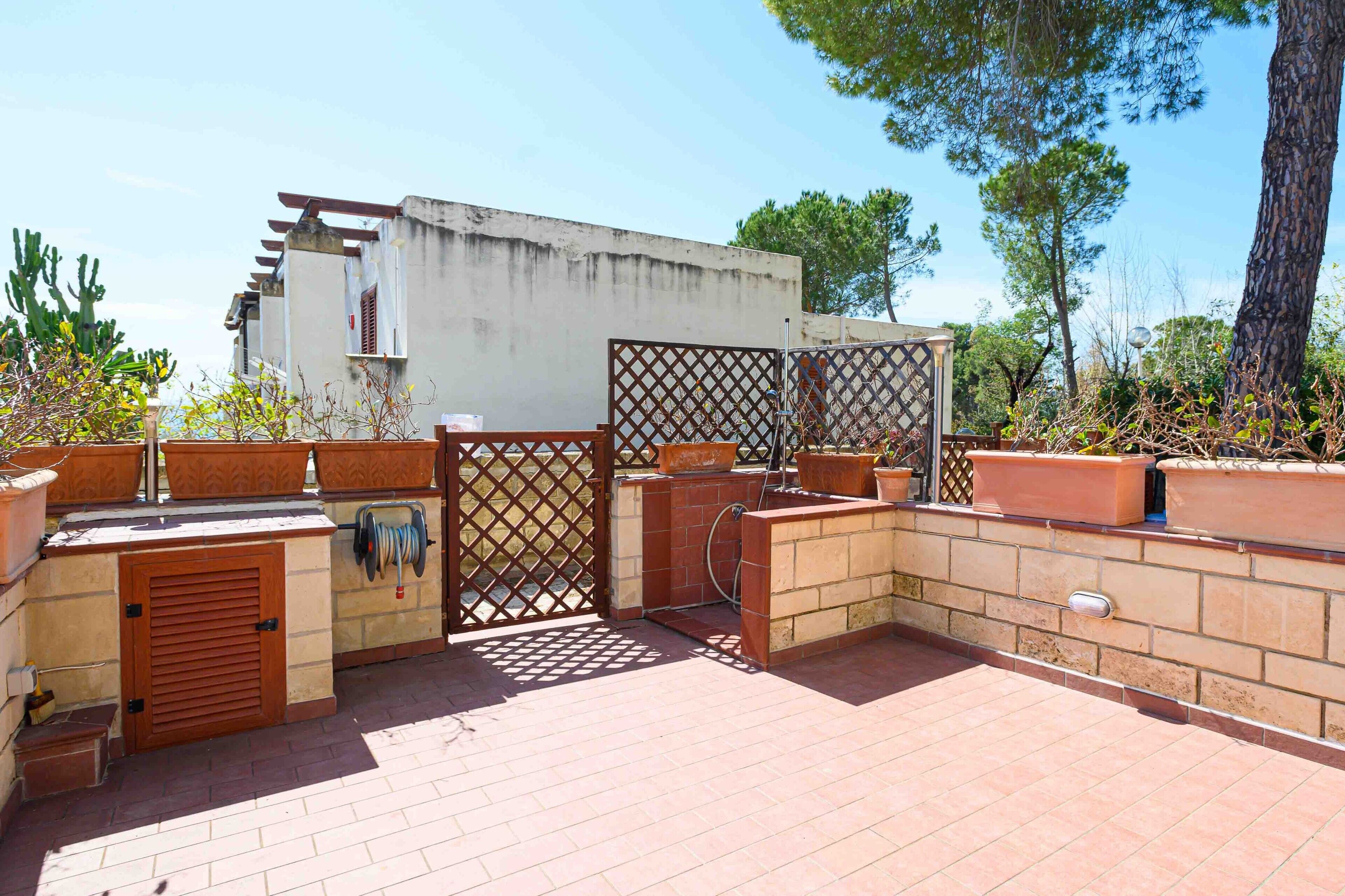 A patio area with a grill, potted plants, and a wooden gate.
