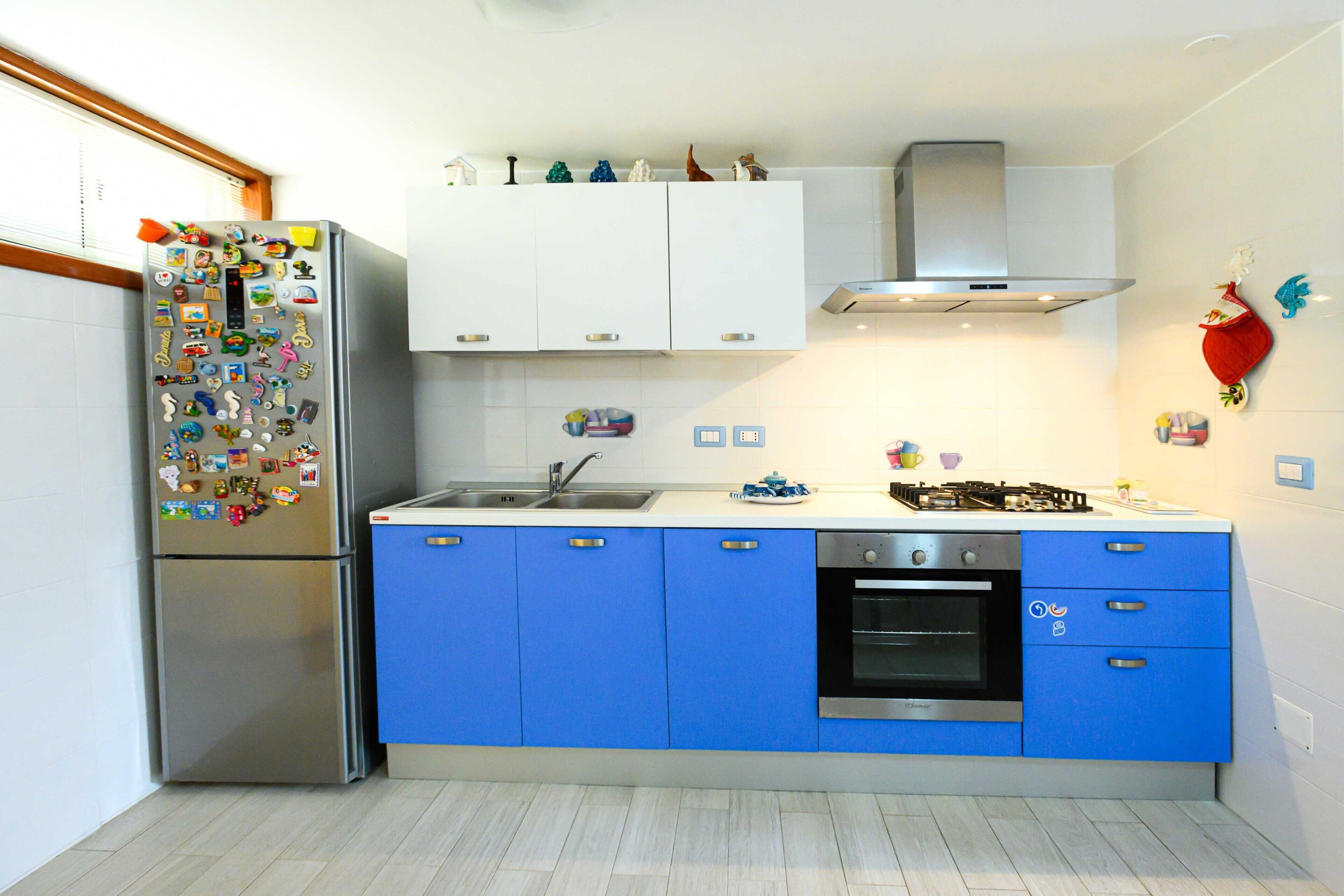 A modern kitchen with a stainless steel refrigerator, blue cabinets, a gas stove, and a built-in oven.