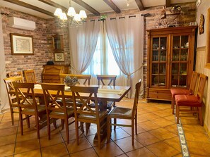 A dining area with a wooden table and chairs, a chandelier, a brick wall, and a cabinet with glass doors. - Villa 'Del Monte Casa Rural' with Mountain View, Wi-Fi and Air Conditioning (Navahermosa)