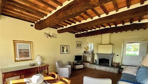 Un soggiorno con camino, travi in legno, televisione e zona pranzo.