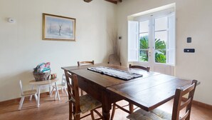 A dining area with a wooden table, white chairs, a framed picture, and a window with a view of greenery. - Villa 'Ringo' with Private Pool, Private Garden and Wi-Fi (Capannori)
