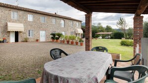 A covered patio area with a table and chairs, a stone building in the background, and potted plants. - Villa 'Ringo' with Private Pool, Private Garden and Wi-Fi (Capannori)