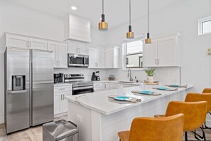 A modern kitchen with white cabinetry, stainless steel appliances, a central island with seating, and pendant lighting.