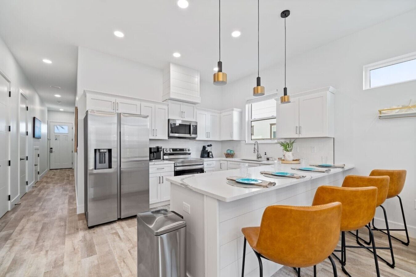 A modern kitchen with white cabinetry, stainless steel appliances, a central island with bar stools, and pendant lighting.
