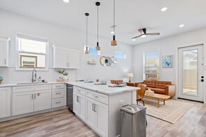 A modern kitchen with white cabinets, a central island, pendant lights, and a ceiling fan.