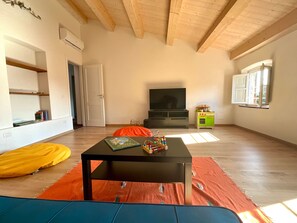 A spacious living room with a wooden ceiling, a flat-screen TV, a small kitchen area, and a sofa.
