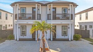 Un edificio residenziale a due piani con balconi, un ingresso centrale e una piccola palma in primo piano.