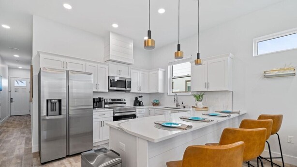 A modern kitchen with white cabinetry, stainless steel appliances, a central island with bar stools, and pendant lighting. - 5BDR~Heated Pool+Golf Cart+Grill+Pool Table (Panama City Beach)
