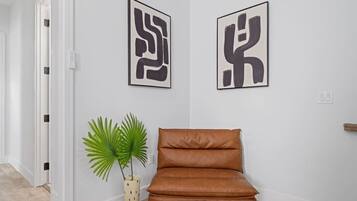 Ein Flur mit einem braunen Ledersessel, einer Kübelpflanze und zwei abstrakten Kunstwerken an der Wand.