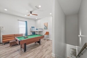 Een kamer met een pooltafel, een bank, een stapelbed en een plafondventilator.