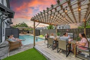 Um quintal com piscina, área de estar externa e um pergolado com luzes de cordão.