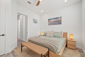 A bedroom with a bed, bedside lamps, a bench, and a door.
