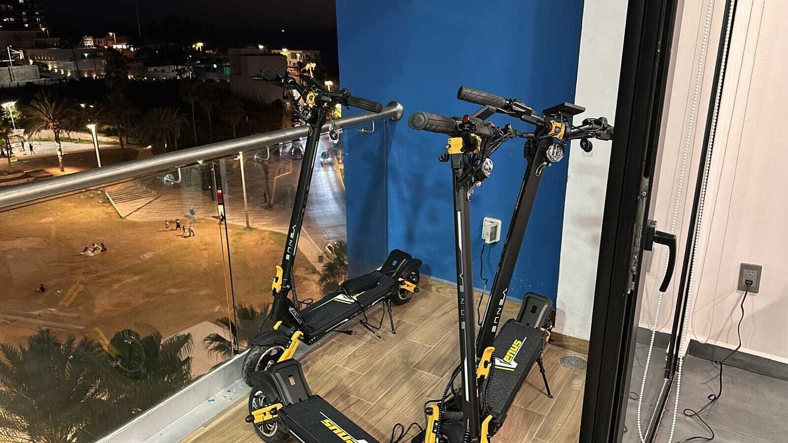 A balcony with two electric scooters and a view of a parking lot at night.