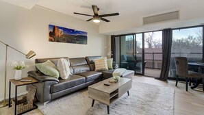 A modern living room with a leather sofa, a coffee table, and a large window with a view of the outdoors. - Downtown City Walk High-Rise 2BR | GYM | Sauna (Colorado Springs)