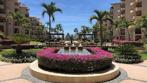 Un complexe hôtelier doté d’une fontaine centrale, entourée de parterres de fleurs et de palmiers.