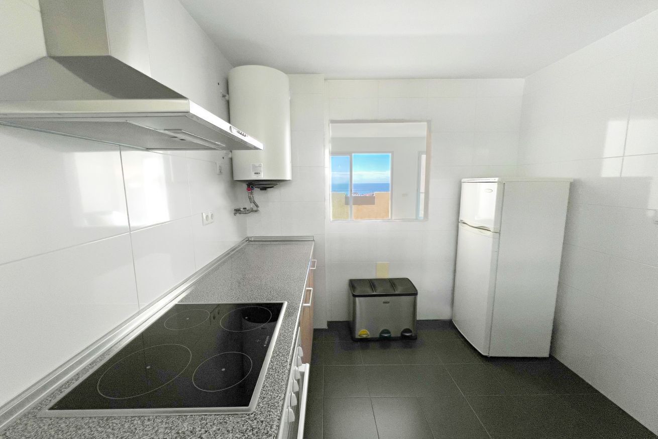 A compact kitchen with a stove, a small trash bin, a refrigerator, and a window with a view.