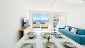 Uma sala de jantar com mesa posta para seis pessoas, um sofá e vista para o mar.