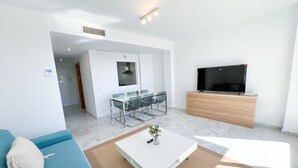 Uma sala de estar moderna com sofá, mesa de centro, TV e área de jantar.